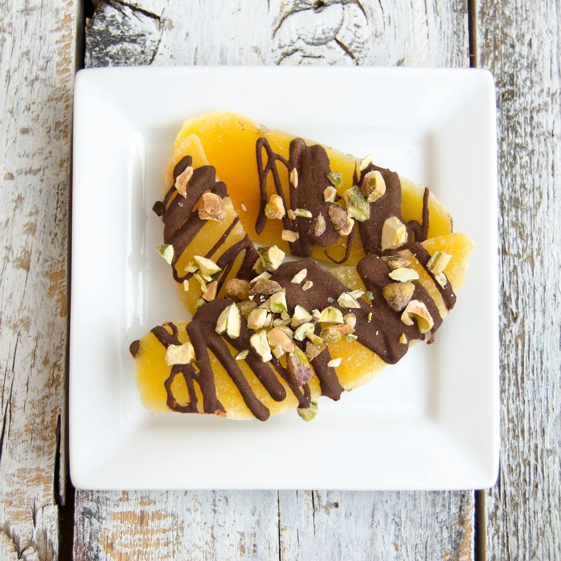 Completed chocolate and pistachios drizzled mangos displayed on a plate